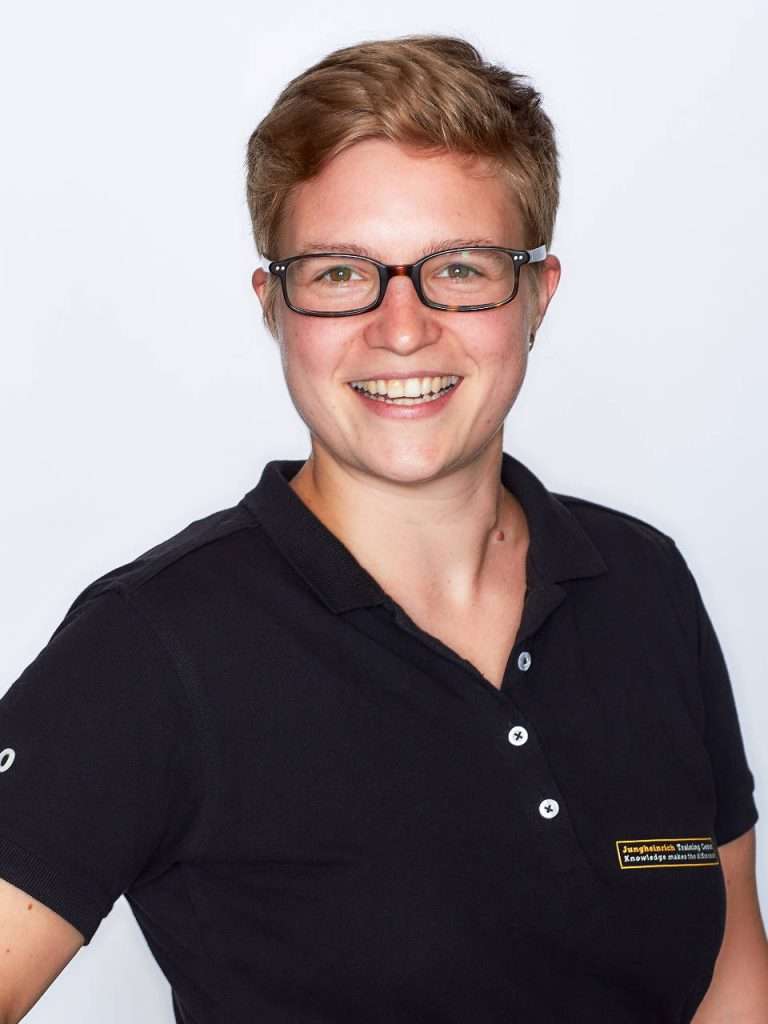 Portraitfoto von Wiebke Peters, die freundlich in die Kamera lächelt. Sie trägt ein schwarzes Poloshirt mit einem Logo von Jungheinrich Training Center und vermittelt einen professionellen und offenen Eindruck. Wiebke Peters ist Ansprechpartnerin beim Kunden Jungheinrich und hat ein Feedback zur Ausbildung interner Trainer gegeben.